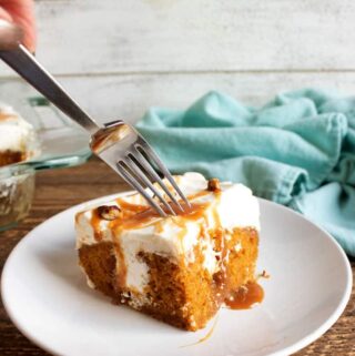 pumpkin poke cake on white plate with blue towel in the background and a fork poking into the cake