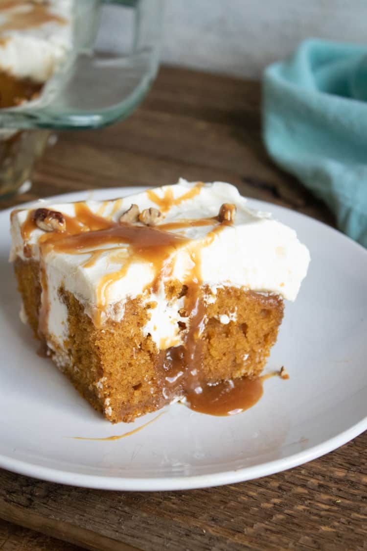 pumpkin poke cake on white plate with blue towel in the background