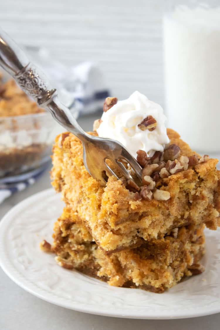 fork lifting a bite of pumpkin dump cake topped with whipped cream and pecans