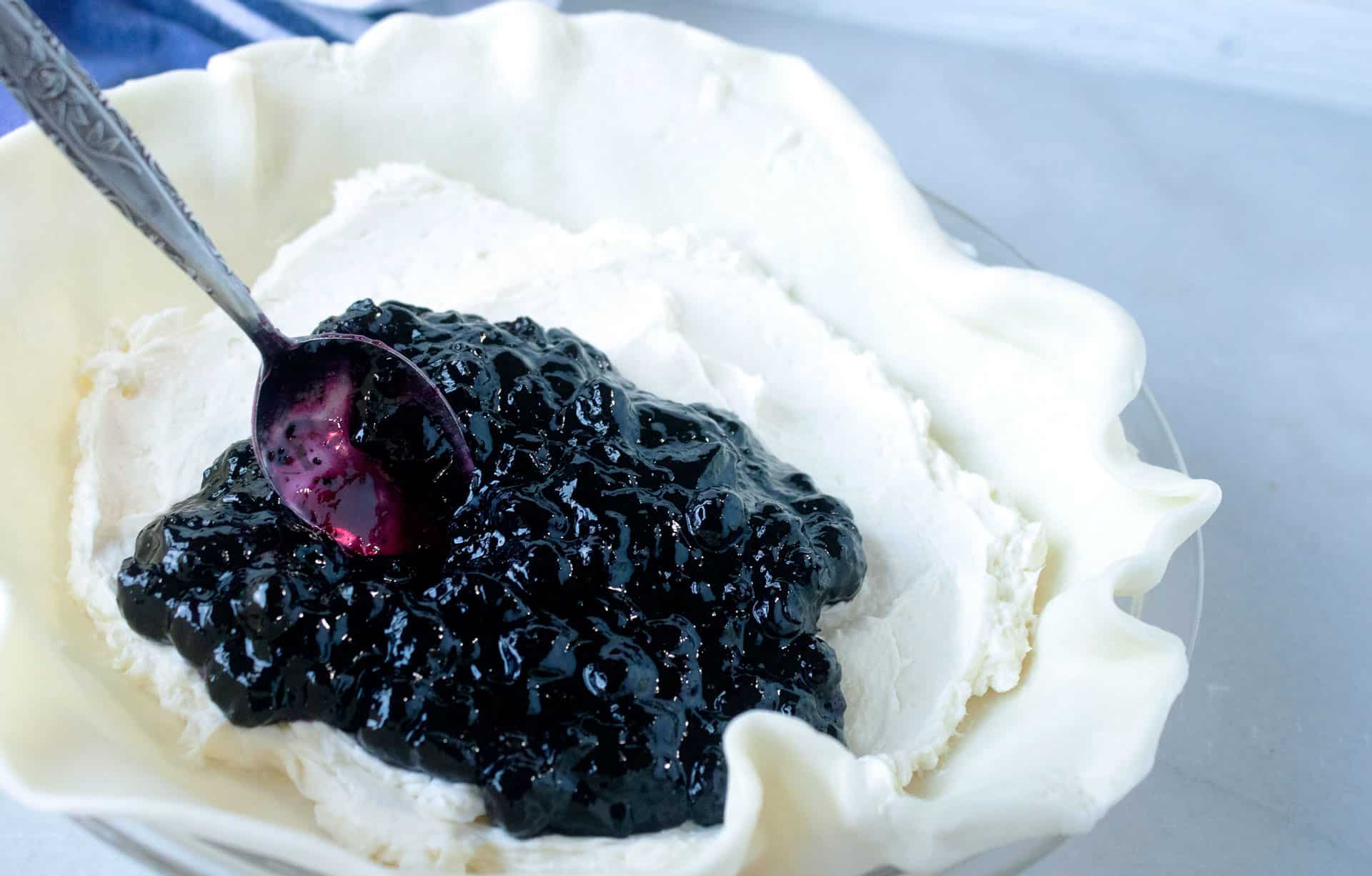 spoon spreading blueberry preserves over cream cheese in a pie shell