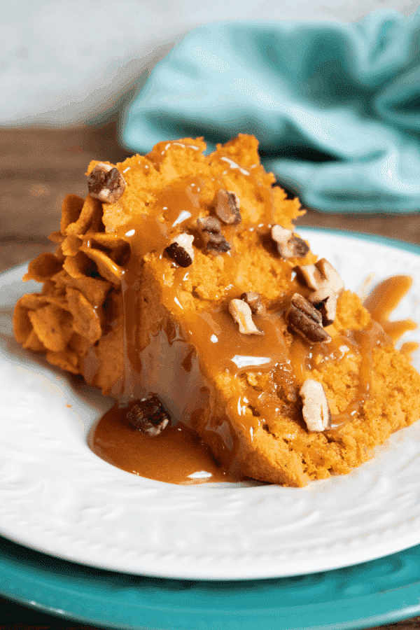 Slice of layered pumpkin cake with pumpkin ganache filling, caramel sauce, and pecans on a white plate