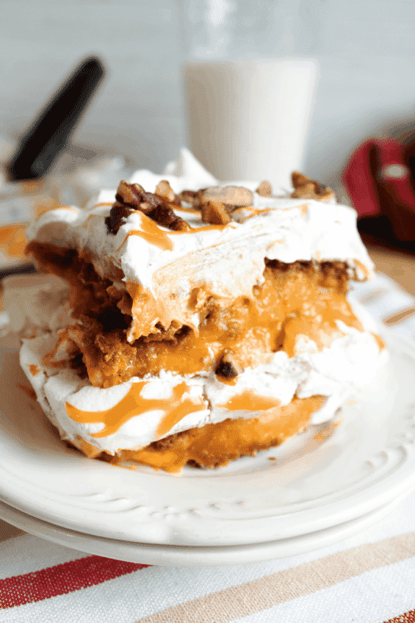 A slice of no-bake pumpkin lasagna dessert on a white plate, topped with caramel sauce and chopped pecans
