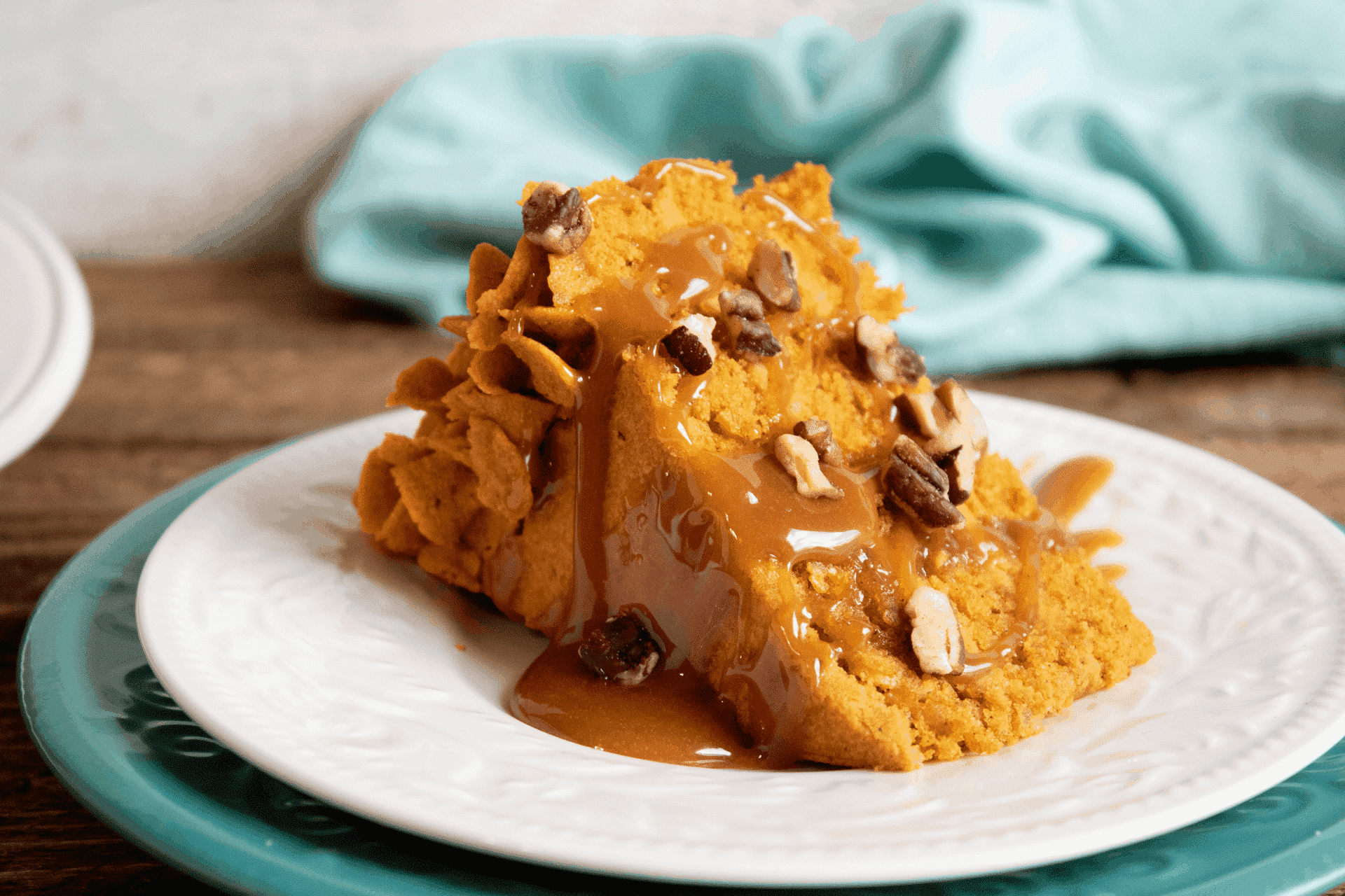 Slice of layered pumpkin cake drizzled with caramel sauce and topped with chopped pecans on a white plate