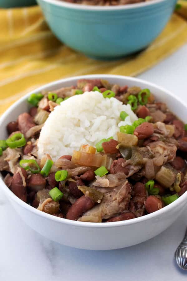 Slow cooker Popeyes red beans and rice with ham hock meat, white rice and scallions in a white bowl