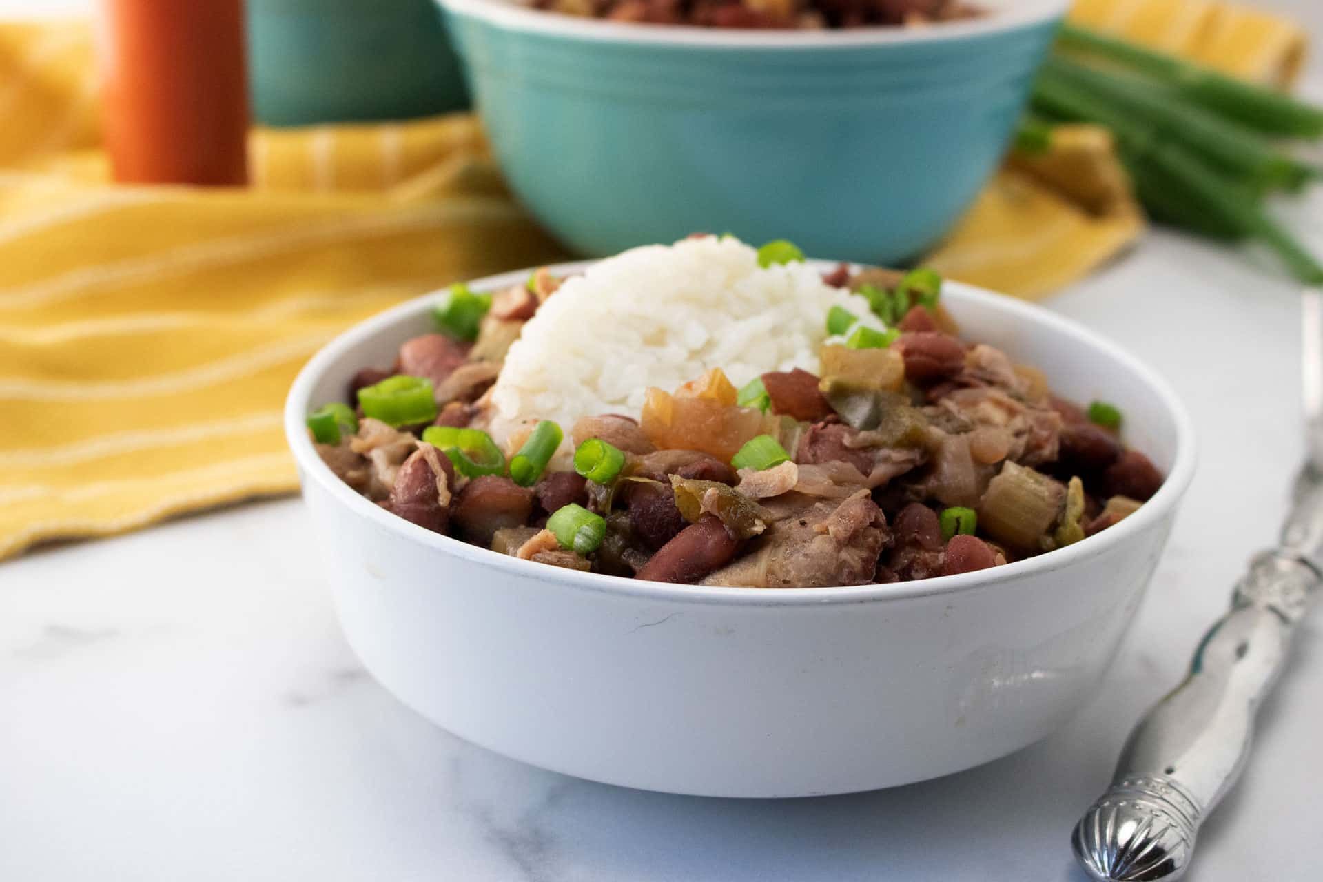 Bowl of Popeyes-style red beans and rice with scallions, fork and a bowl of beans behind it