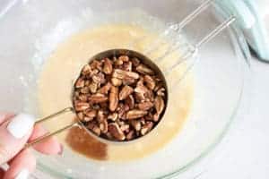 measuring cup with pecans adding to mixing bowl for derby pie ingredients