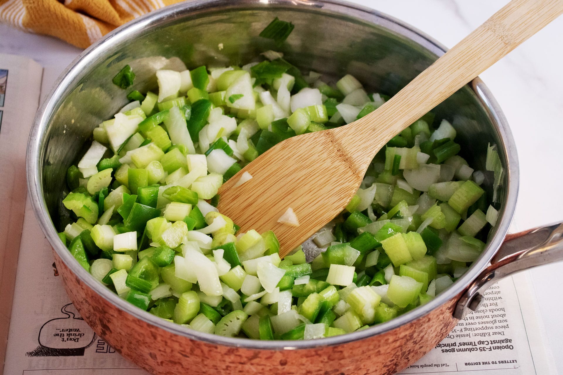 Diced vegetables sauteing in a copper skillet with a wooden spoon