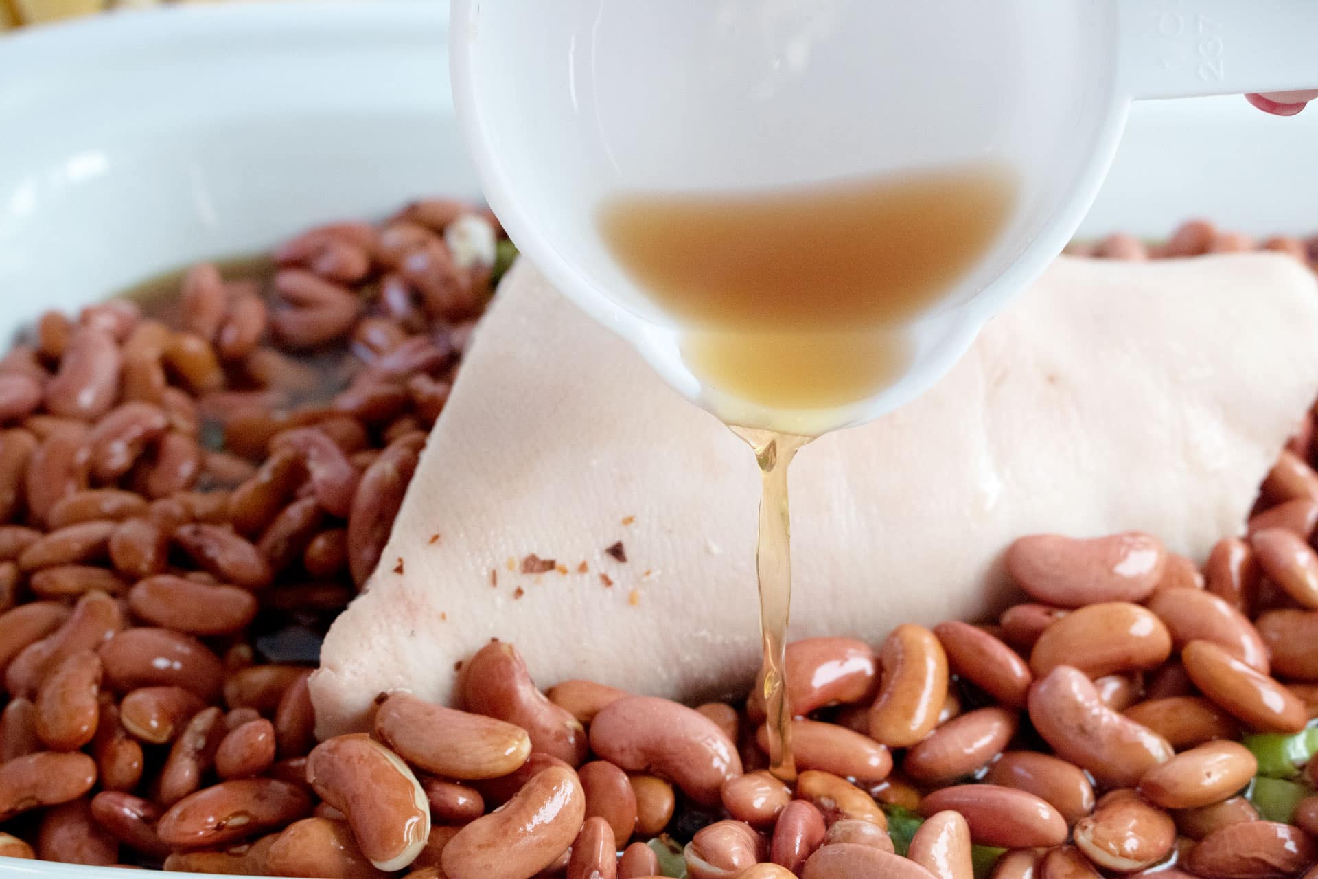 Beef broth pouring over red beans and a ham hock in the slow cooker