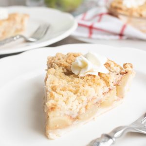 slice of apple crumble pie on white plate with green apples in the background