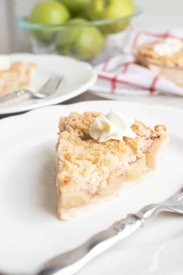 slice of apple crumble pie on white plate with green apples in the background