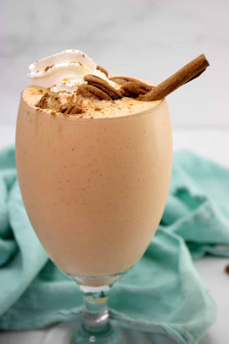 Close-up of a pumpkin cheesecake milkshake topped with whipped cream, pecans and a cinnamon stick