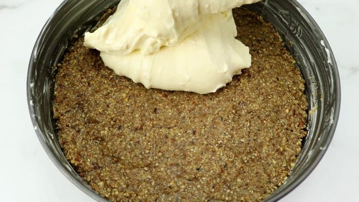 pouring cheesecake filling over pecan crust