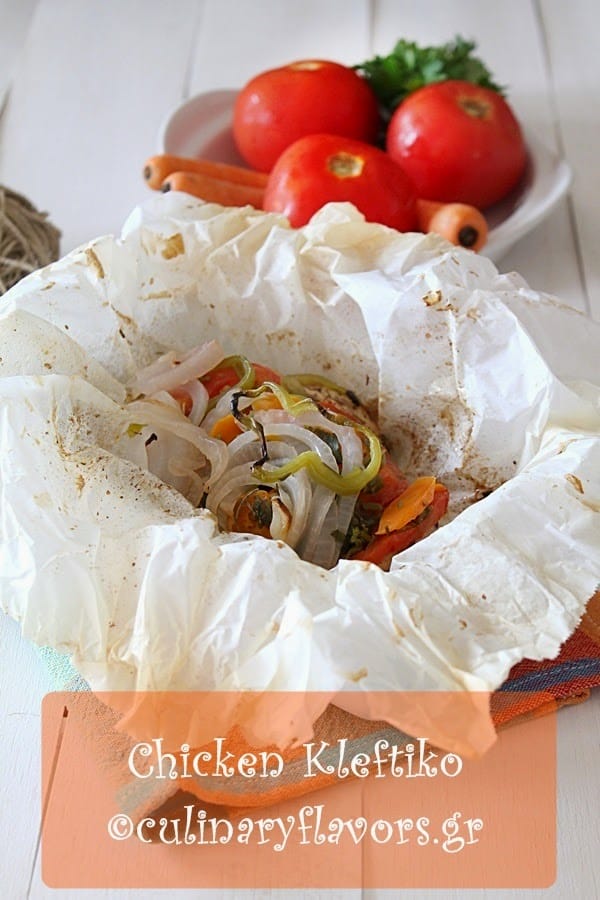 Greek chicken kleftiko in a parchment paper packet topped with onion, green pepper, tomato and carrot slices