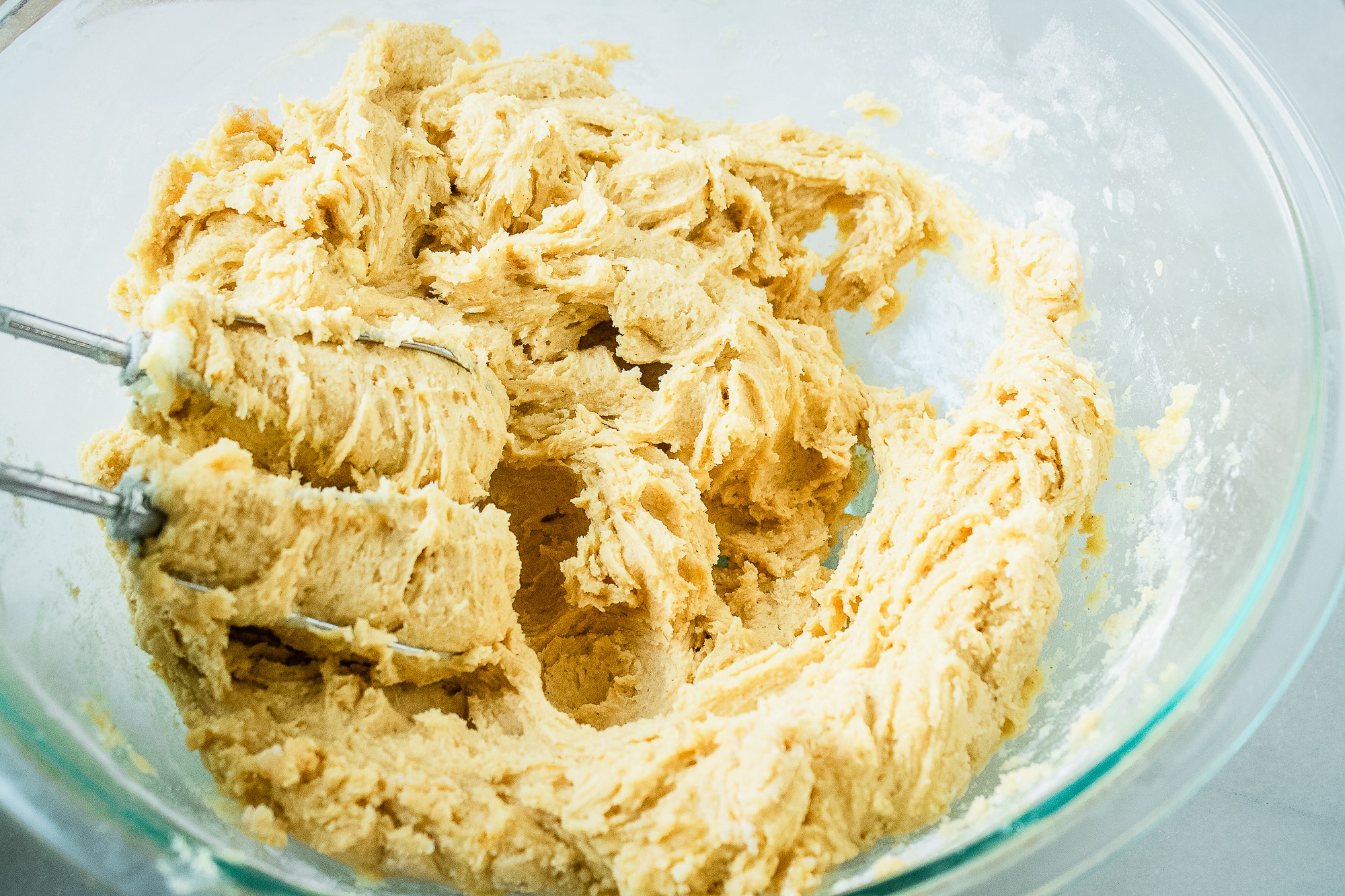 Creamed pumpkin snickerdoodle cookie dough in a glass mixing bowl with beaters