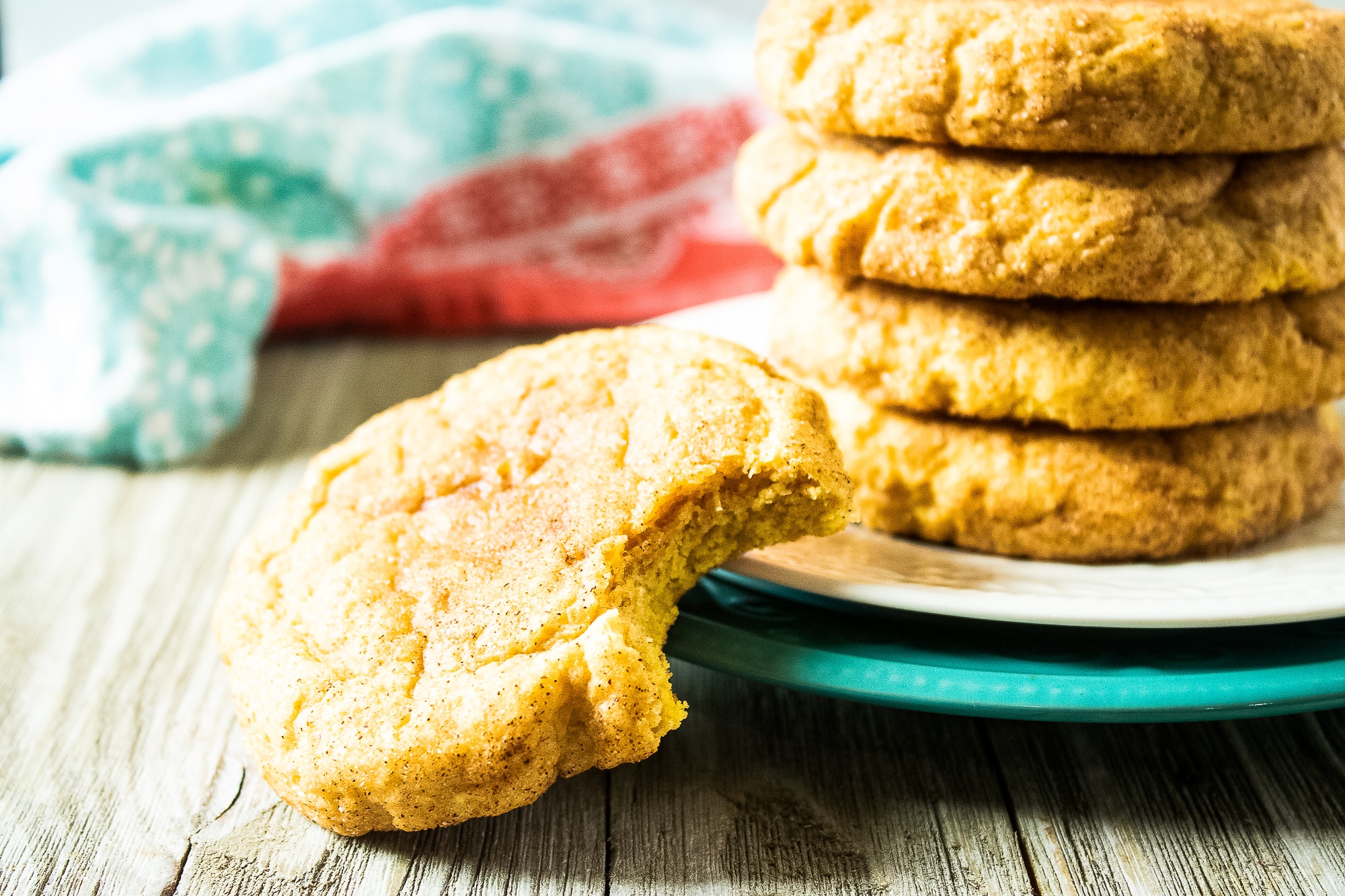 Pumpkin snickerdoodle cookie with a bite taken out of it in front of a stack of cookies