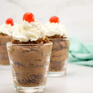 chocolate mousse in three glass dishes with whipped cream and cherry on top
