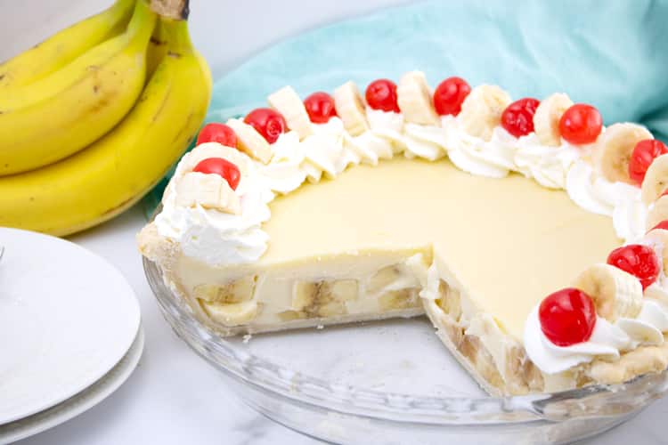 banana cream pie with whipped cream around the edges and banana slices and maraschino cherries decorating the edges