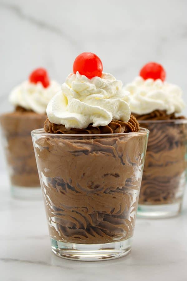chocolate mousse in glass dessert dishes with whipped cream and cherry on top