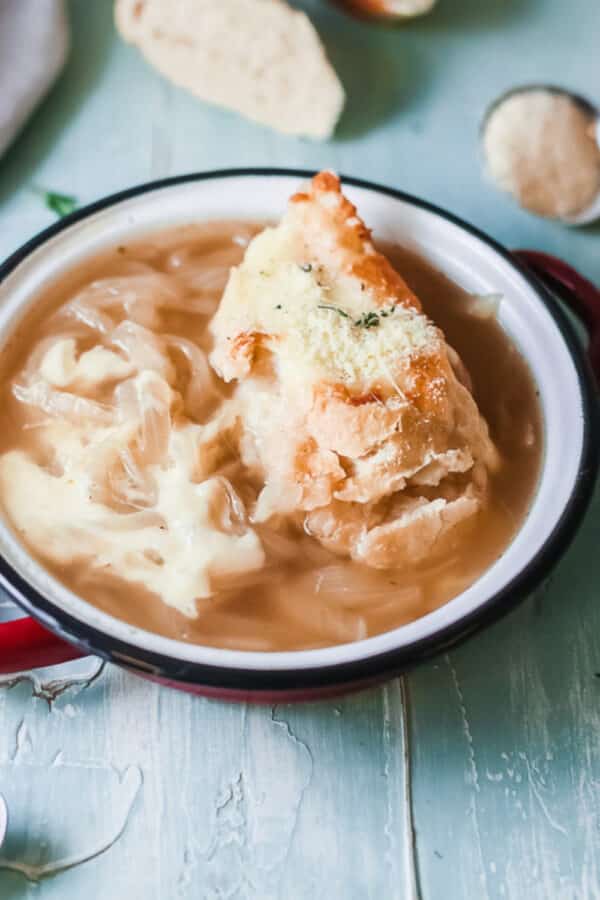 Close-up of copycat Panera French onion soup with a cheesy toasted baguette in a red bowl