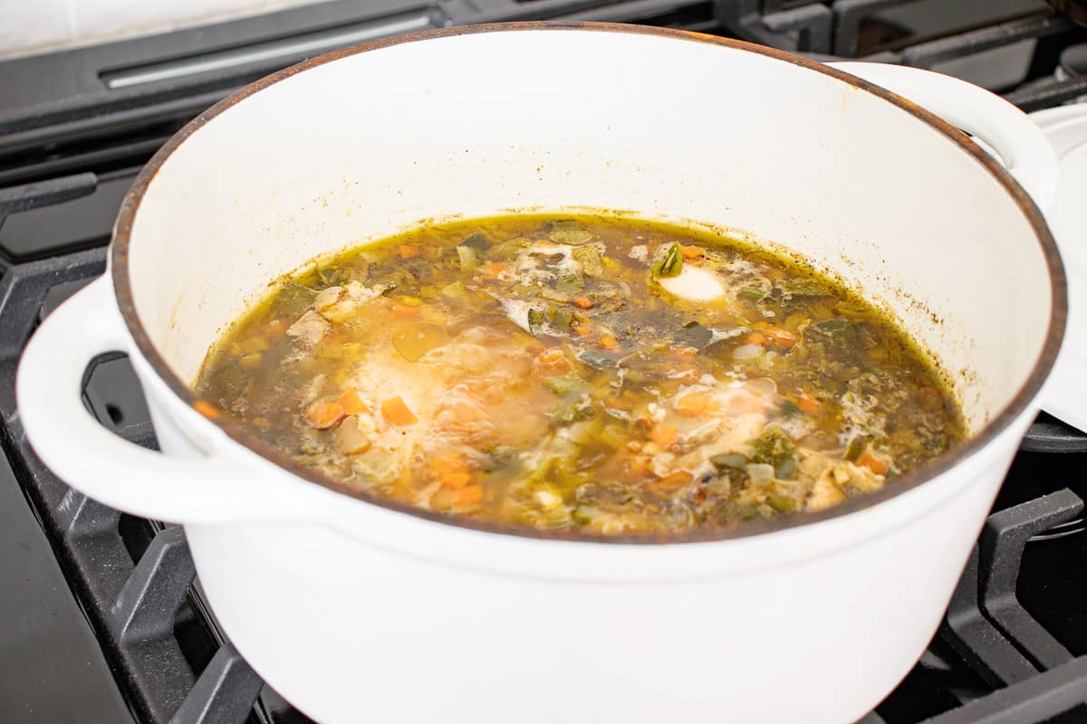 Chicken breasts simmering in poblano vegetable broth in a white Dutch oven