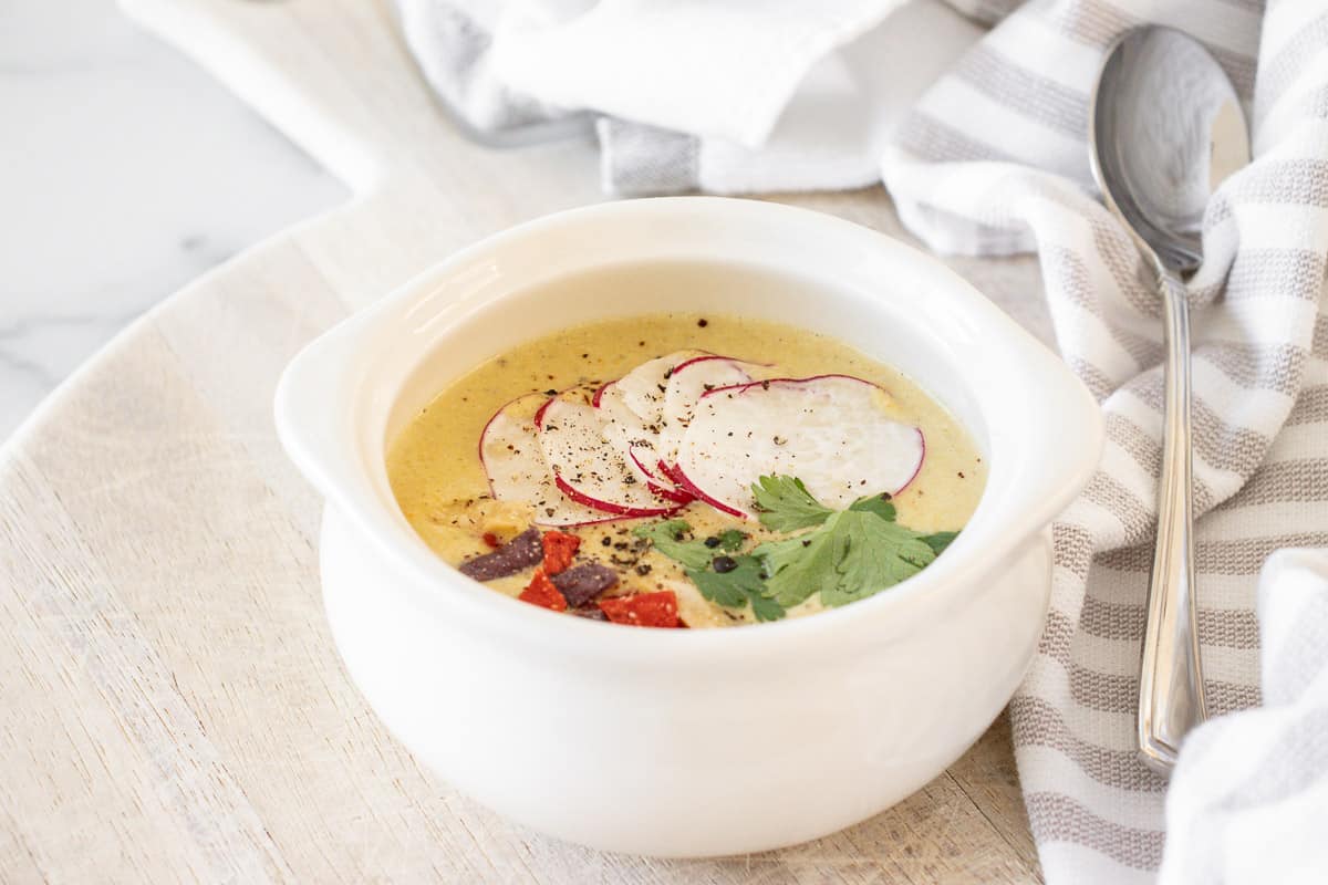 Creamy chicken poblano soup in a white bowl with radishes, cilantro and tortilla strips