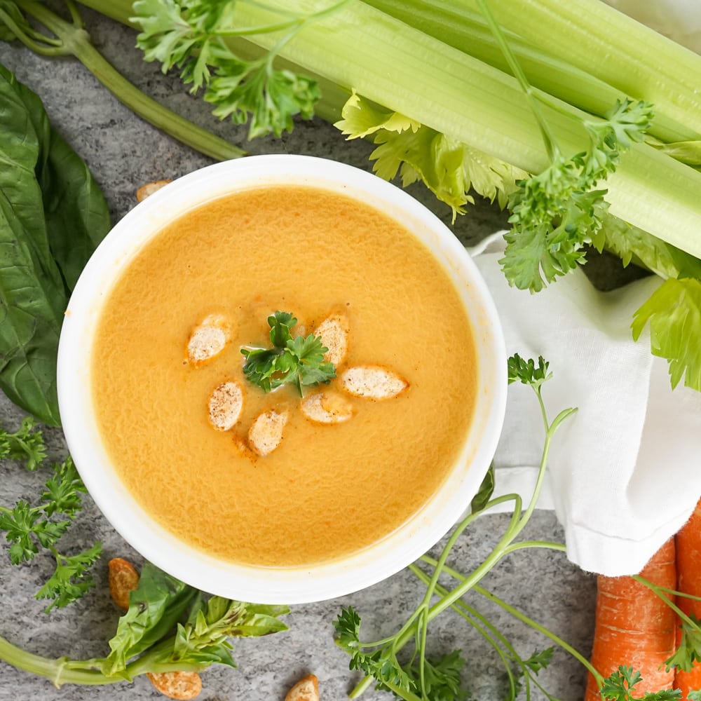 Overhead view of creamy autumn squash soup in a white bowl topped with toasted pumpkin seeds