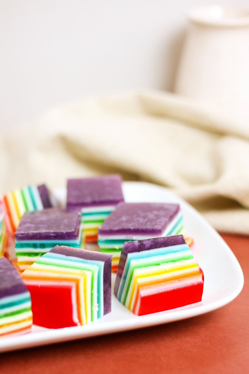 squares of rainbow layered jello on white plate and orange table