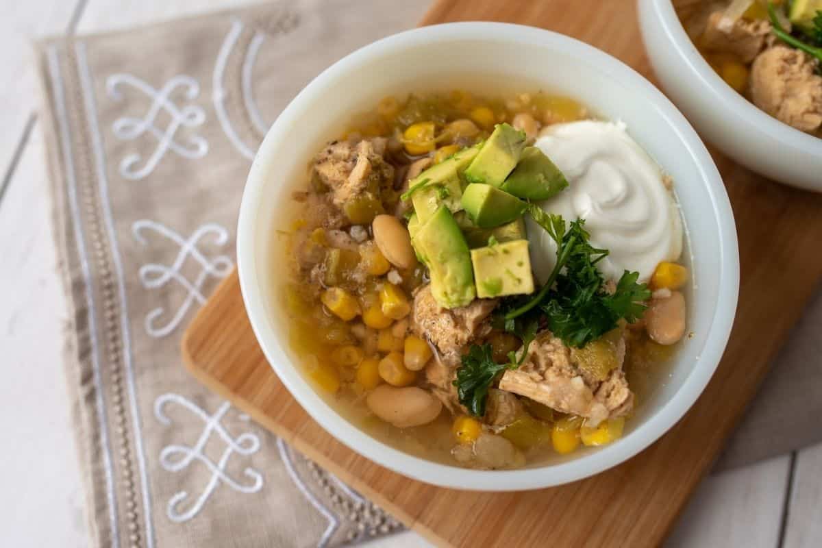 slow cooker white chicken chili being served with avocado and sour cream on top