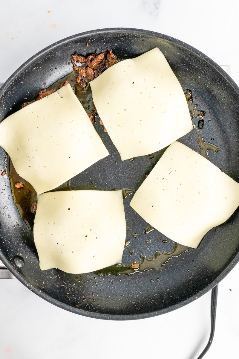 cooking burgers in a skillet with cheese slices on top