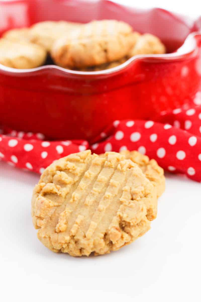 old-fashioned peanut butter cookie on white table in front of red plate with more cookies