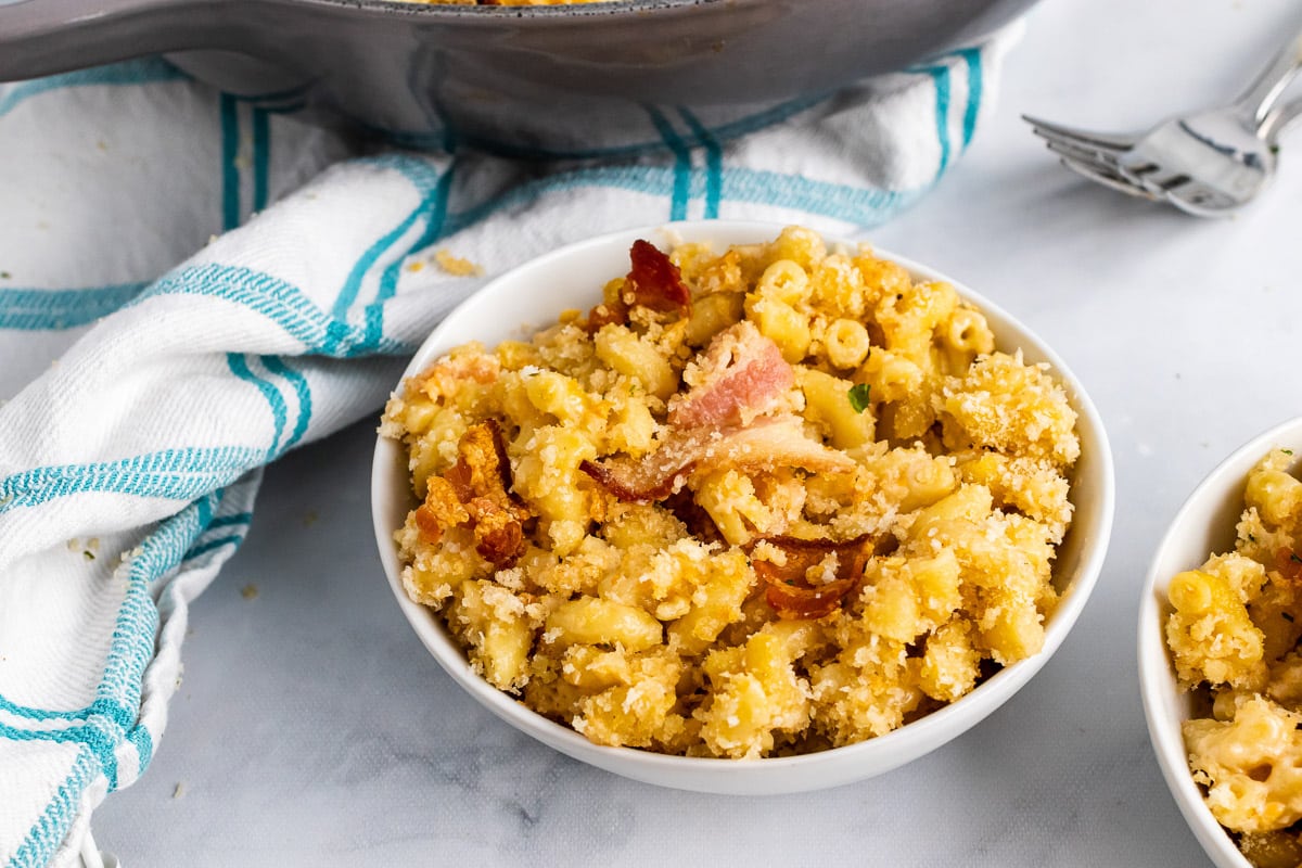 a bowl of bacon mac and cheese in front of a white and blue dish towel