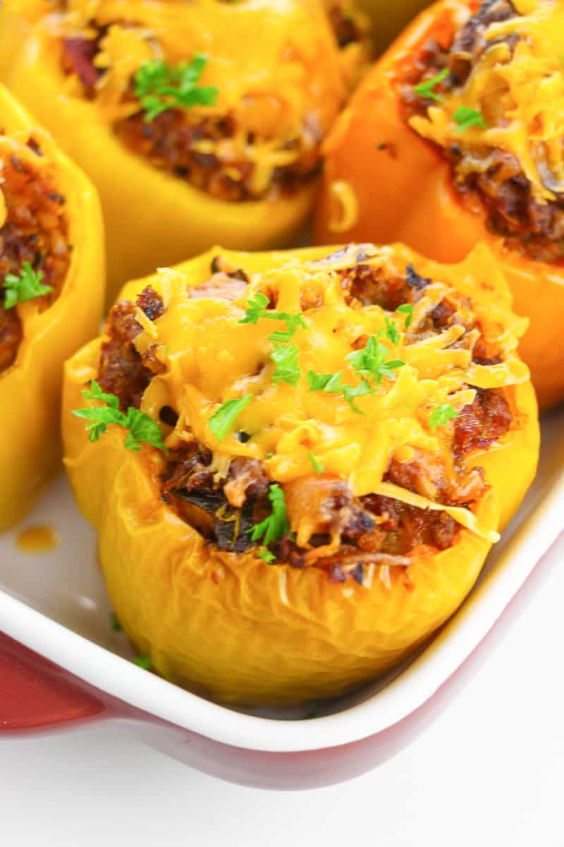 close up keto stuffed pepper with more behind on white tray, topped with cheese and greens