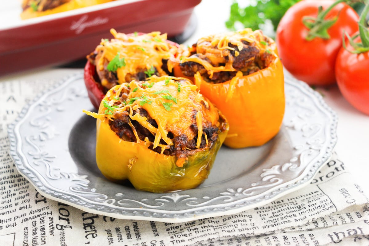 red, orange, and yellow keto stuffed peppers on a white plate with vegetables in the background