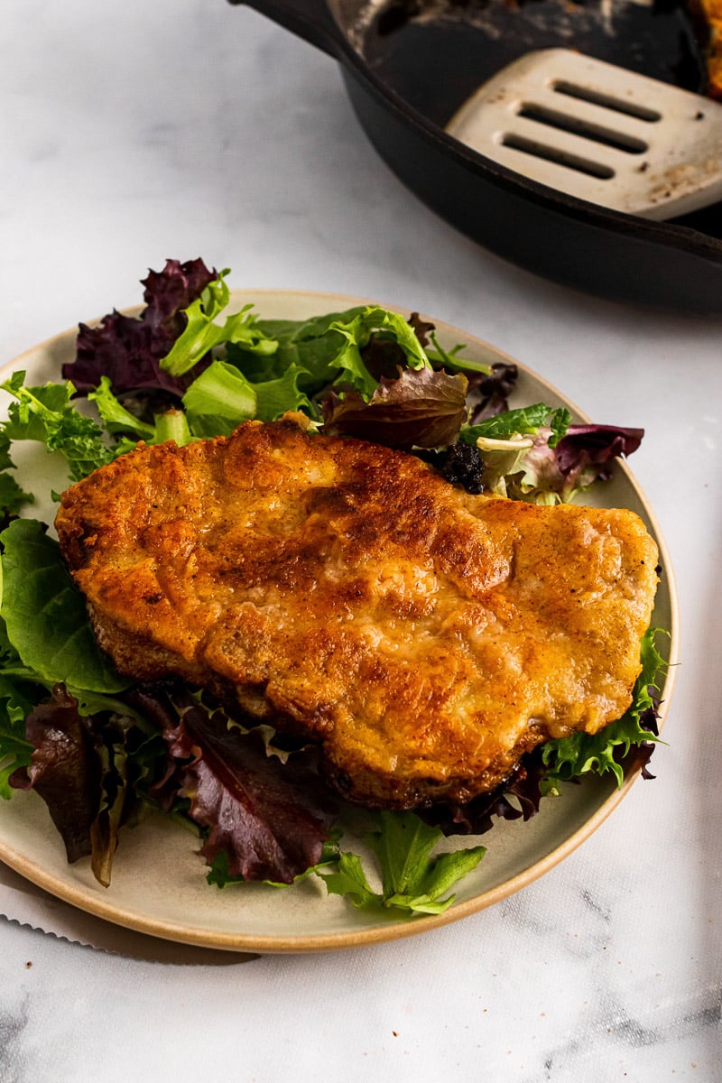 crispy golden southern fried pork chop on a bed of lettuce on a plate