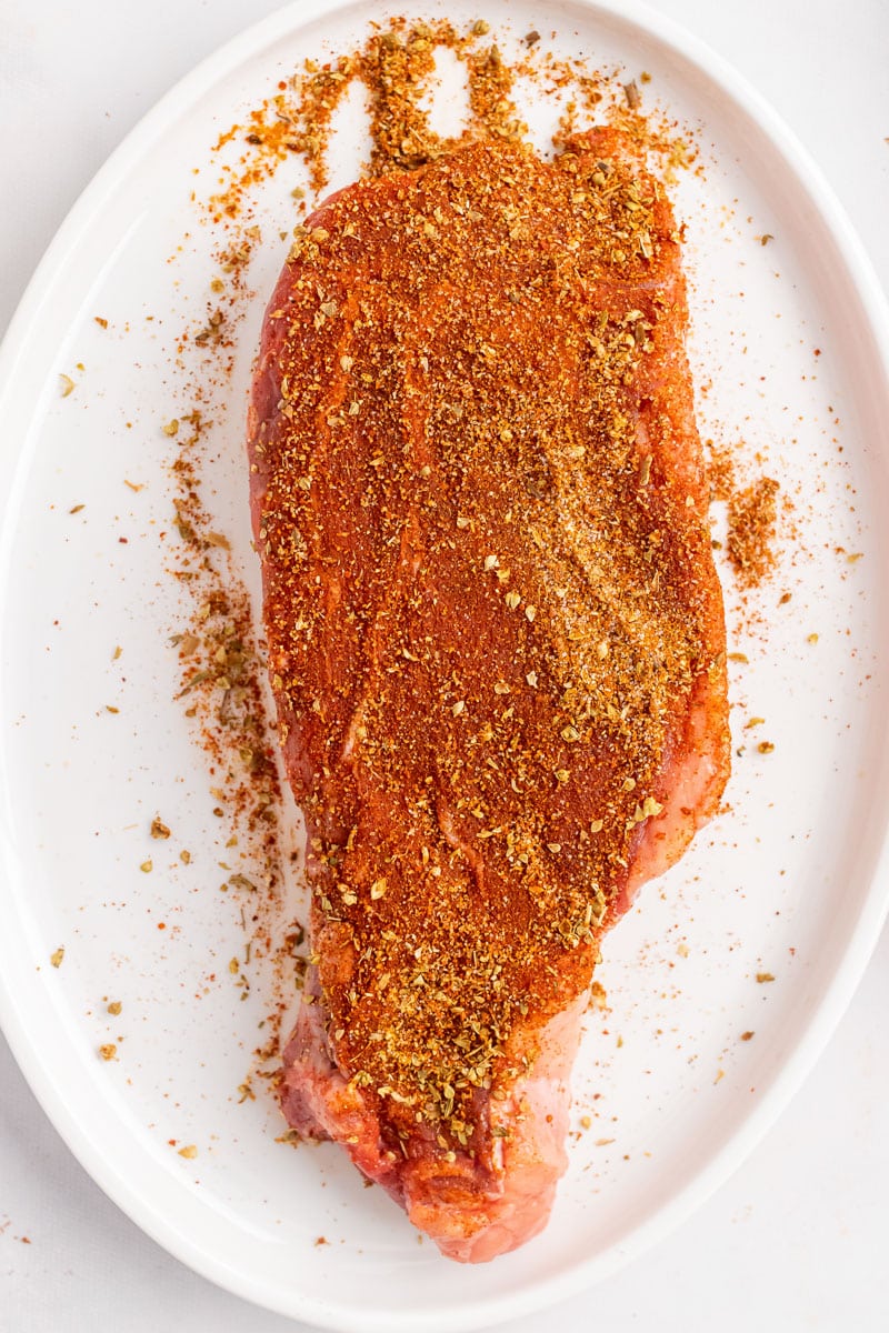 steak rubbed with seasonings on a white plate getting ready to cook in skillet