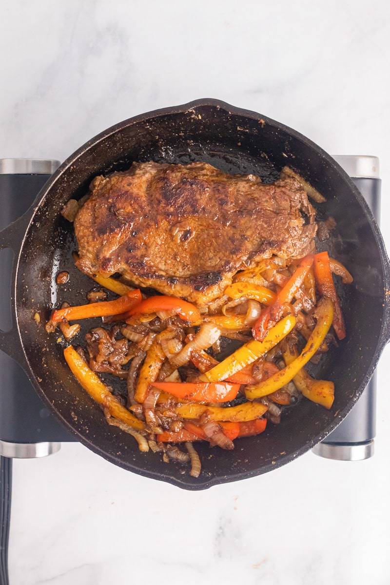 top view of steak in a skillet with cooked peppers and onions