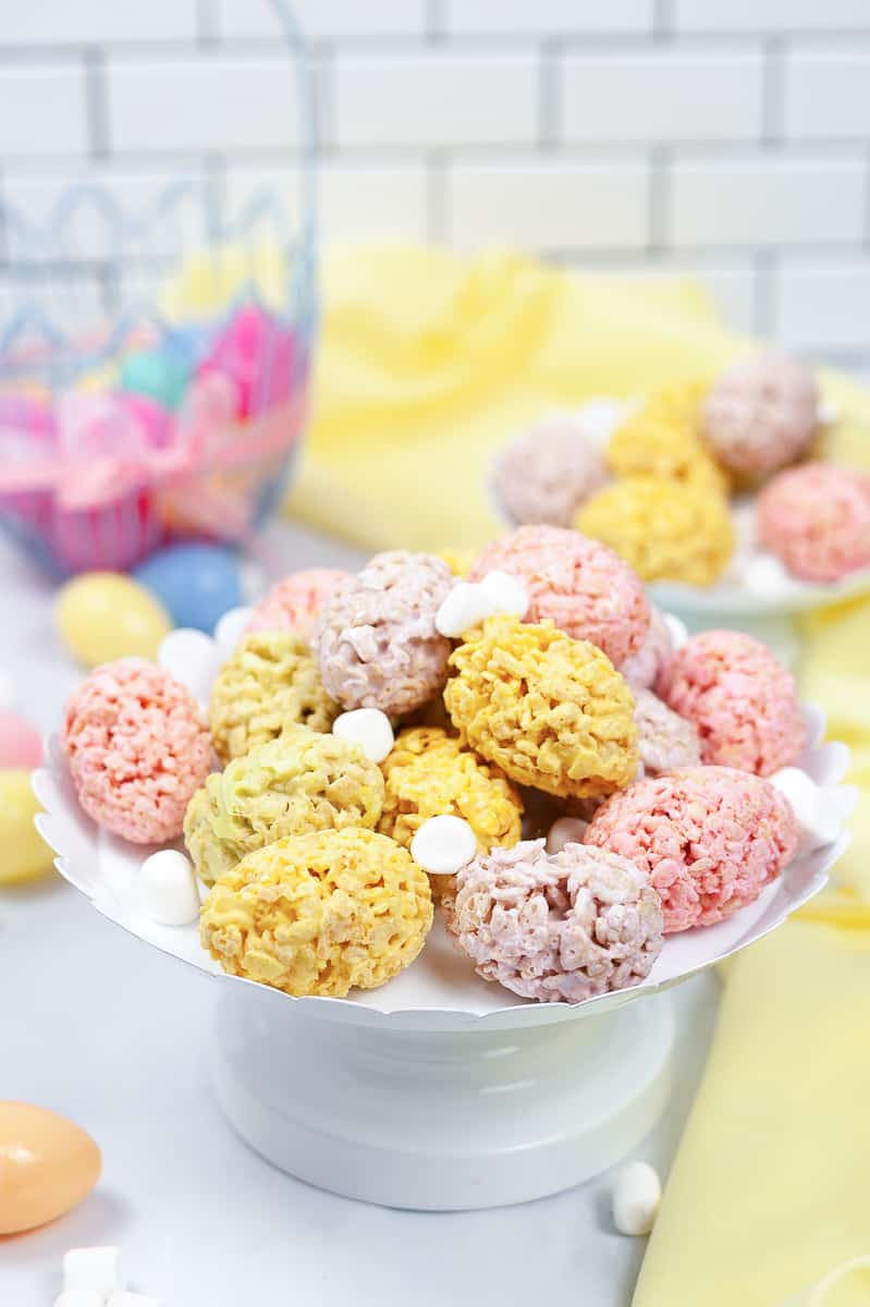 pink, purple, and yellow easter rice krispie treats on a white serving platter with plastic Easter eggs in the background