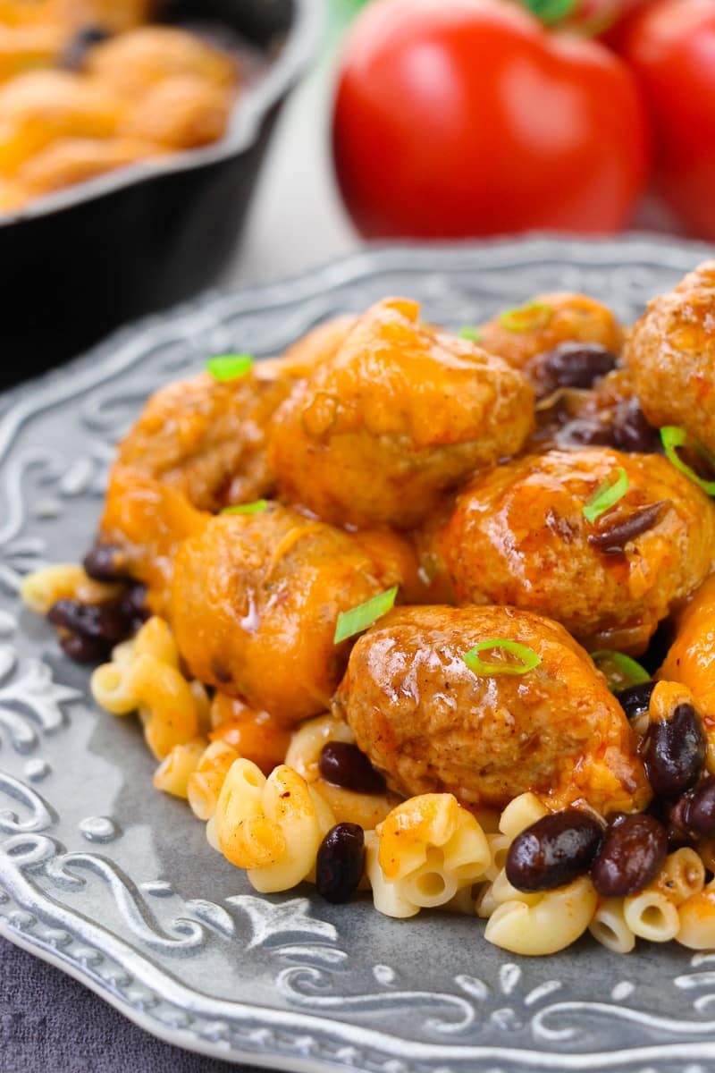 close up of cheesy enchilada meatballs served over macaroni pasta on a gray textured plate