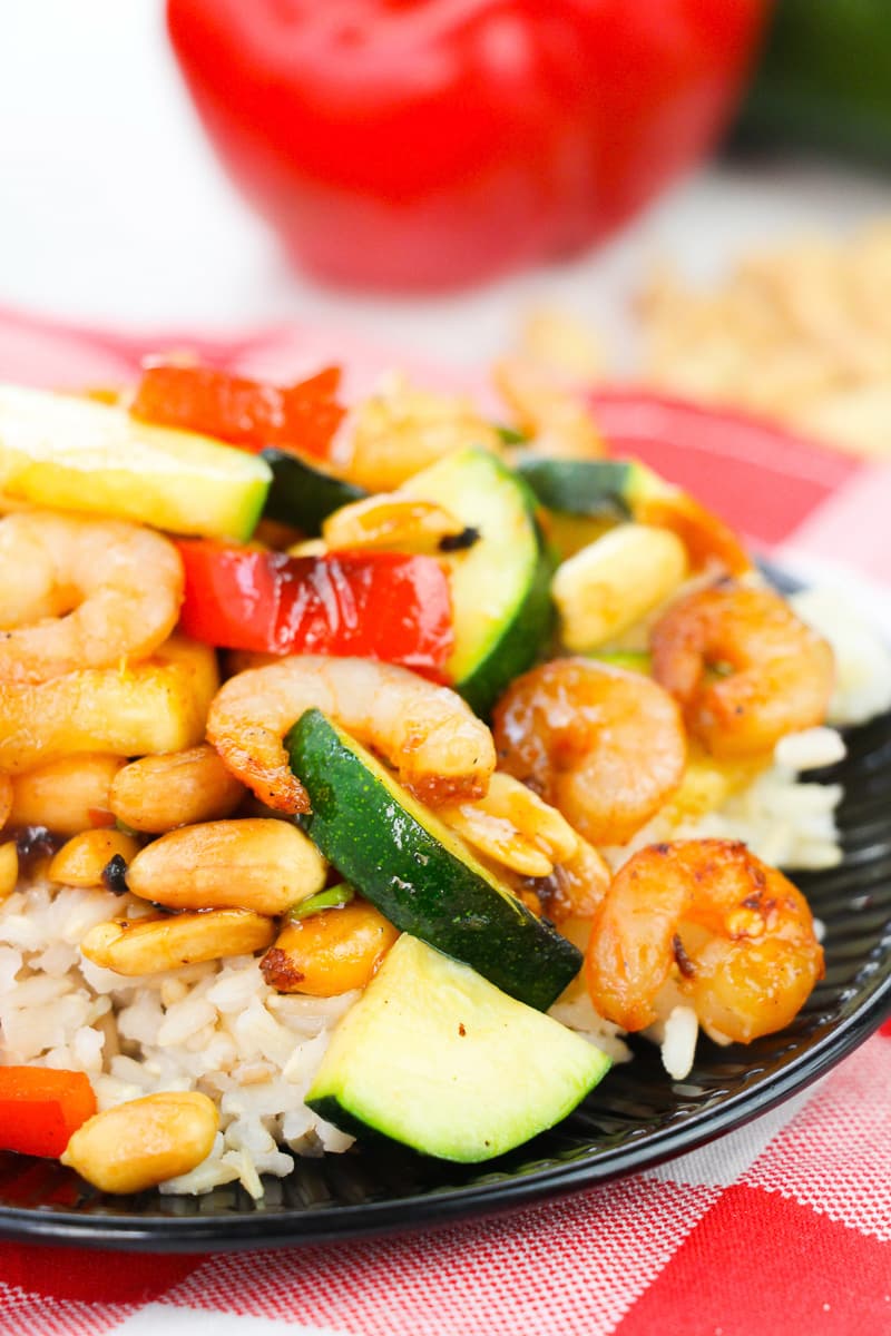 slice up of kung pao shrimp served over rice on dark green plate