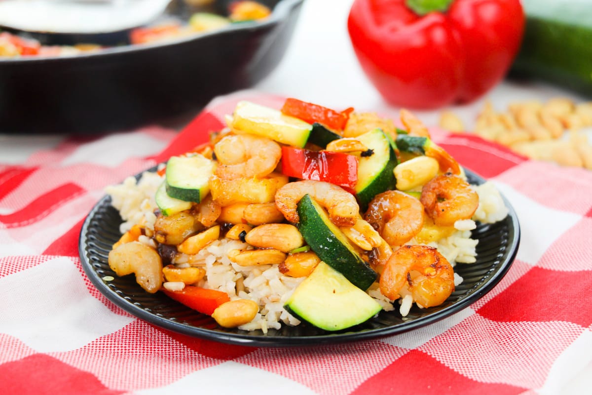 plate of kung pao shrimp served over rice sitting on red checked tablecloth