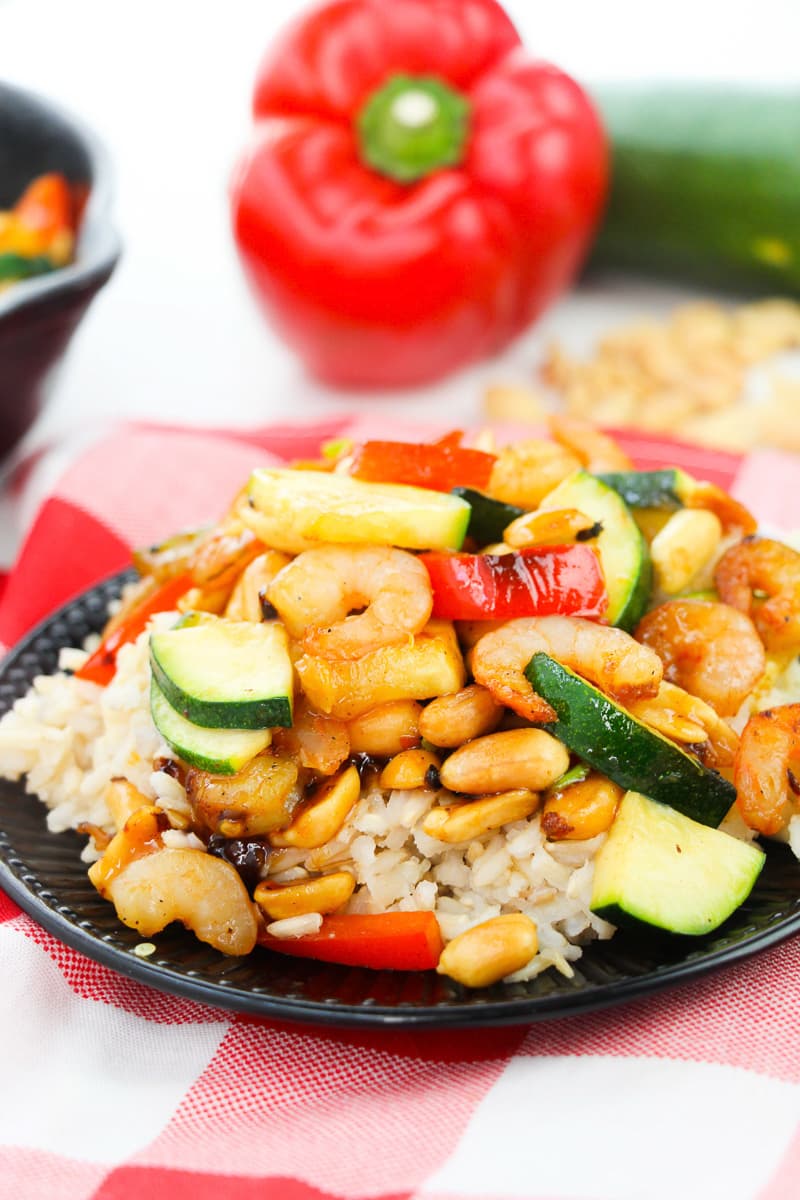 plate of kung pao shrimp served over rice with ingredients in background