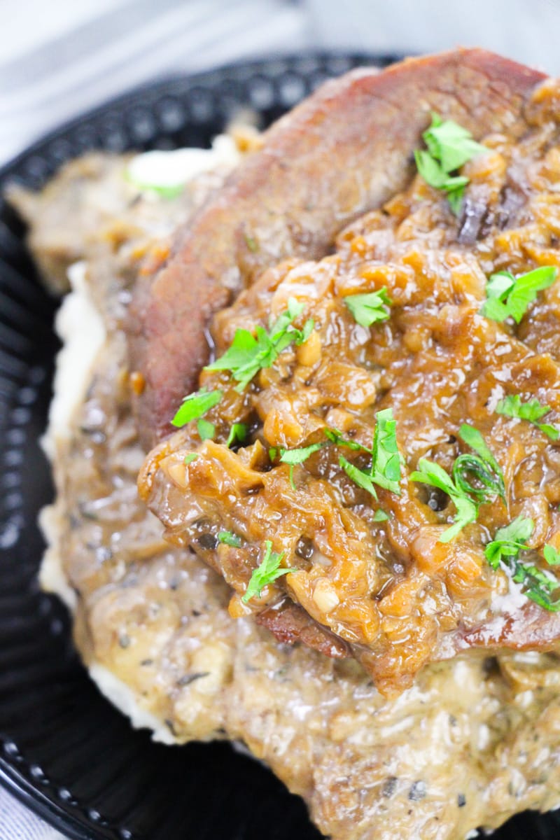 close up top view of easy smothered steak served over mashed potatoes on black plate