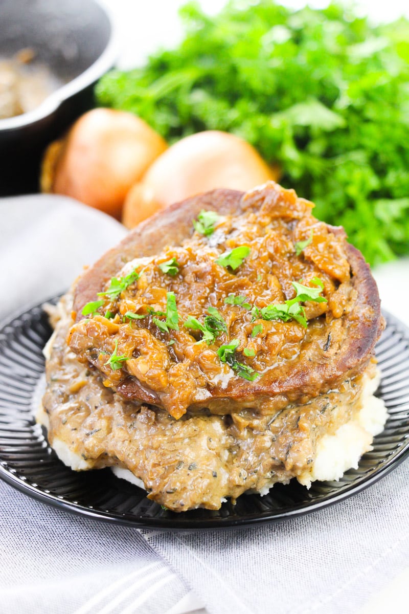 easy smothered steak served over mashed potatoes on a black plate