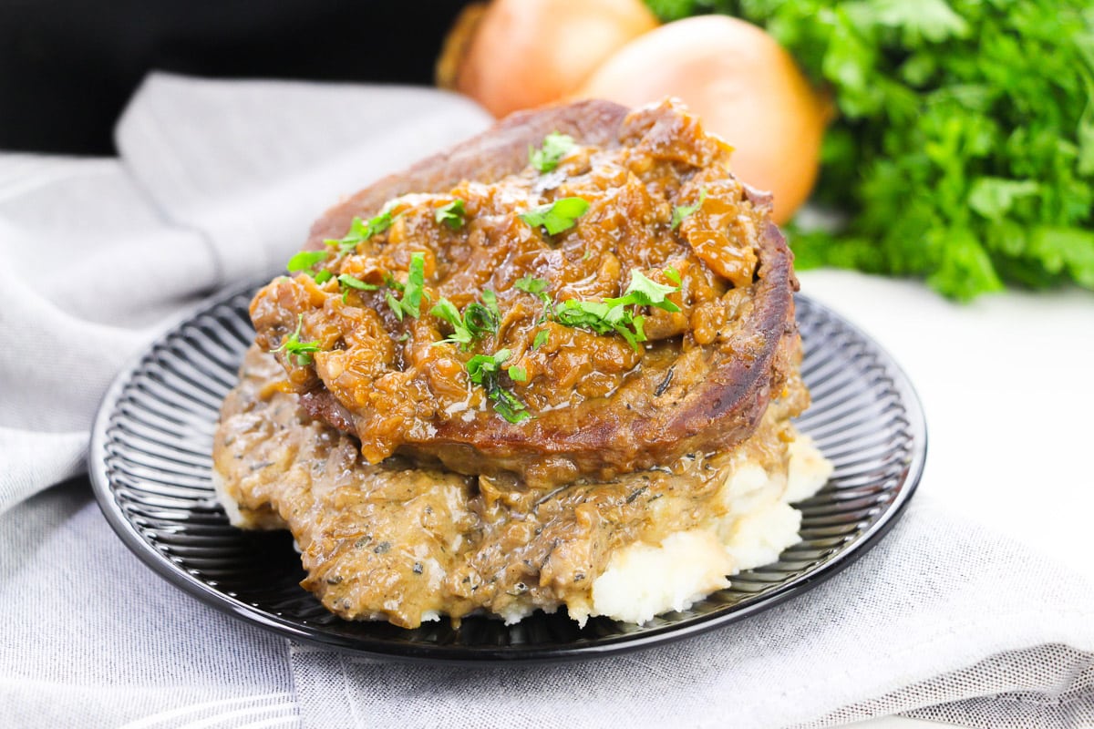 side view of easy smothered steak served over mashed potatoes on a black plate