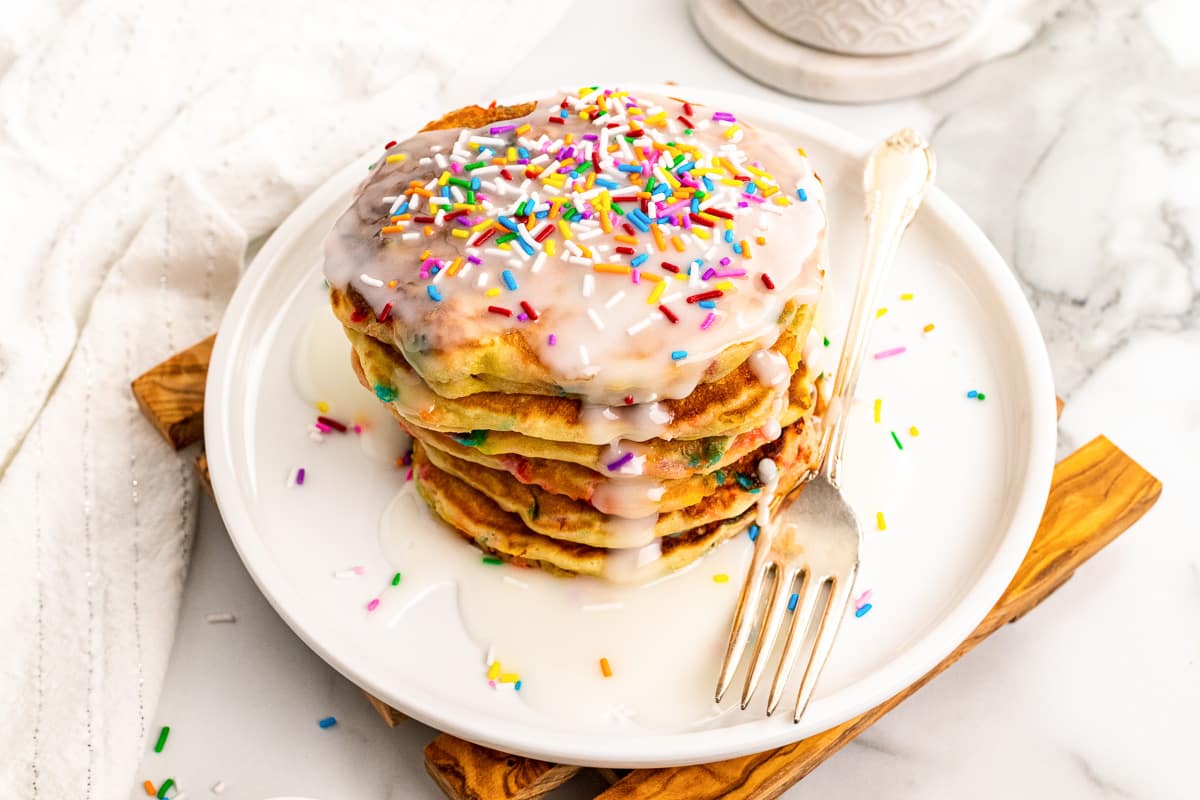 stack of iced funfetti pancakes on white plate with silver fork