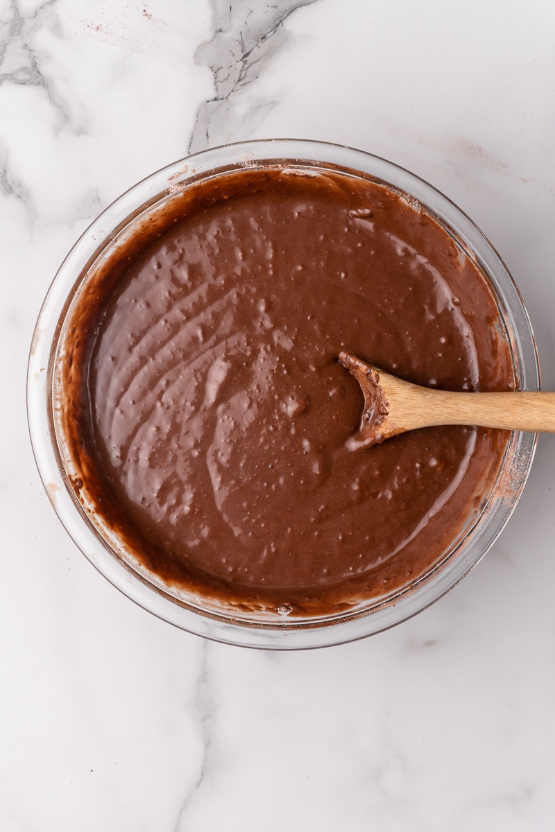 Smooth chocolate cake batter in a mixing bowl with a wooden spoon