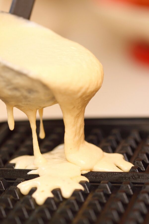 Waffle batter overflowing from a ladle onto a hot waffle iron griddle