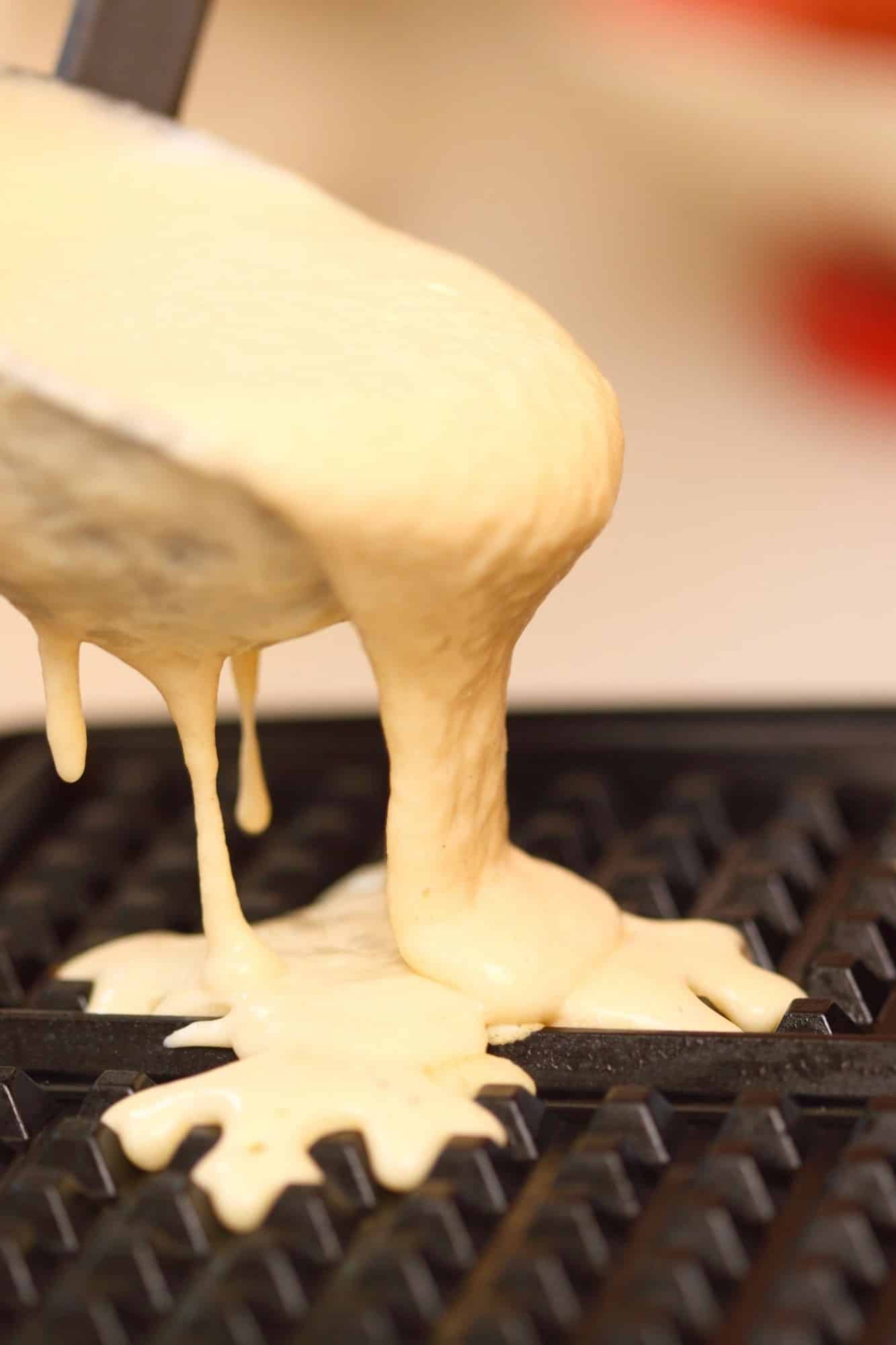 Waffle batter overflowing from a ladle onto a hot waffle iron griddle