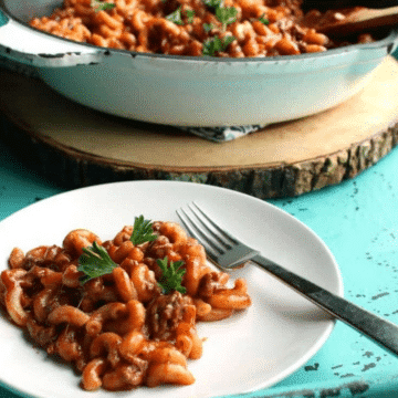 The best chili mac on a white plate with the skillet of chili mac behind it