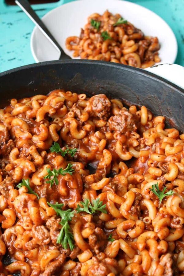 Skillet of chili mac with ground beef and tomato sauce, garnished with fresh parsley
